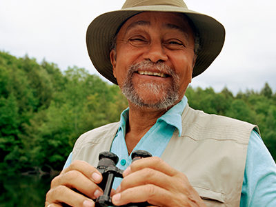 A smiling older man outside holding binoculars