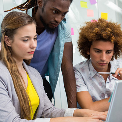 Three young workers surround a computer