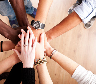 A group of diverse people join hands in cooperation.