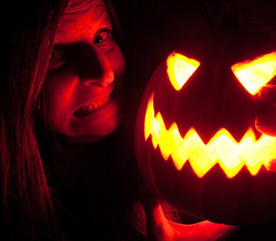 A woman smiling while hodling a jack-o-lantern near her face.