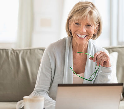 A woman smiling towards you while using a laptop.