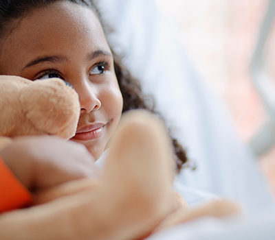 A little girl smiling while holding a teddy bear.