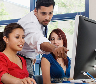 A man pointing out to two women something on a computer screen.