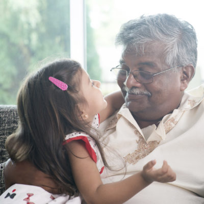 A grandfather and granddaughter smiling at one another.