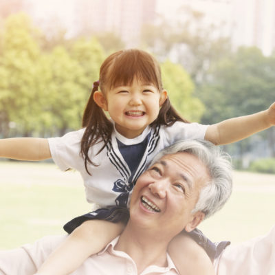 Chinese Grandfather Giving Granddaughter Ride On Shoulders In Park