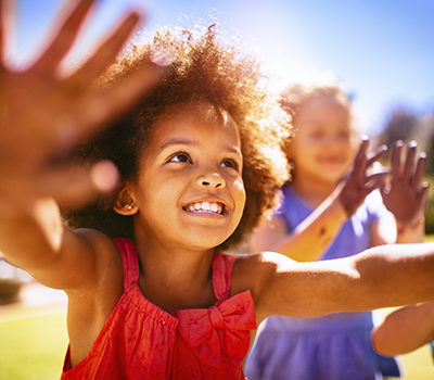 Happy little girl smiling and holding up her hands joyfully in the sun