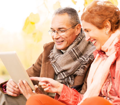 An elderly couple using a tablet in a park