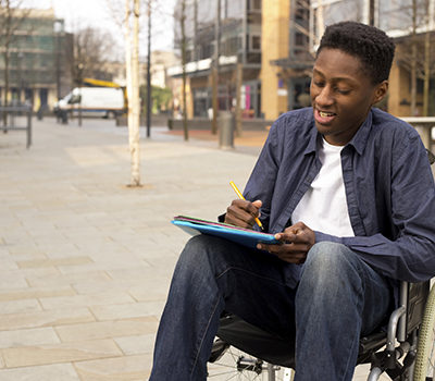 A young man in a wheelchair writing a letter