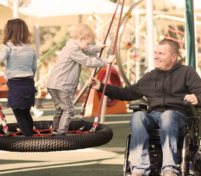 A man in wheelchair pushing kids on a tire swing