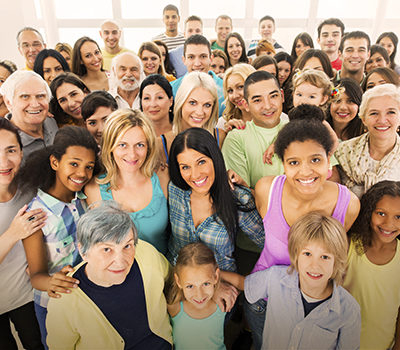 A large group of happy people standing embraced and looking at the camera.