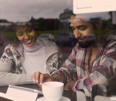 A couple sitting near a window of a coffee shop watching a video on a tablet device