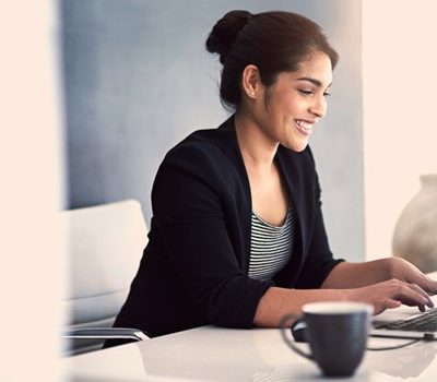 A woman sitting at her desk while smiling and using her laptop