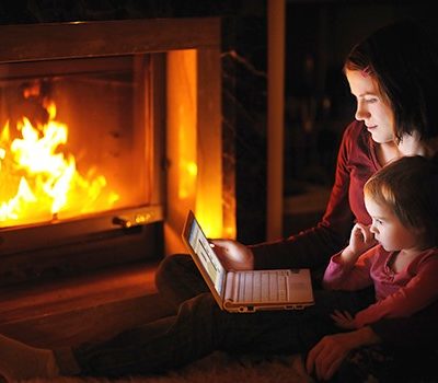 A mother and daughter watching a video on a laptop by fireplace