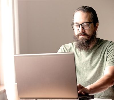 A man sitting at a desk near a window using a laptop