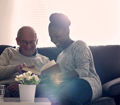 An elderly man and young woman reading on the couch