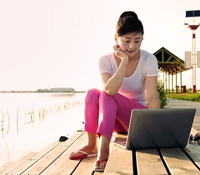 A woman using a laptop while sitting on a set of steps outside by the water