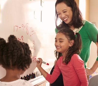 A teacher and students writing on a whiteboard