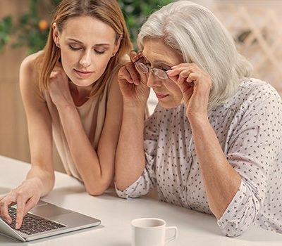 A elderly mother and her daughter sitting at a table and using a laptop