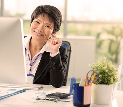 A woman smiling at the camera while sitting in front of her computer at her desk