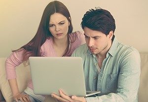 A couple sitting on a couch while using a laptop