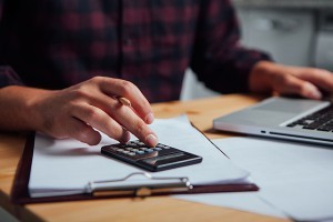 A man doing financies with a calculator, notepad, and laptop