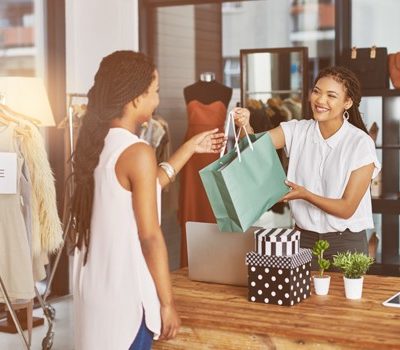 A women at a cash register handing a bag to another woman, completing a transaction