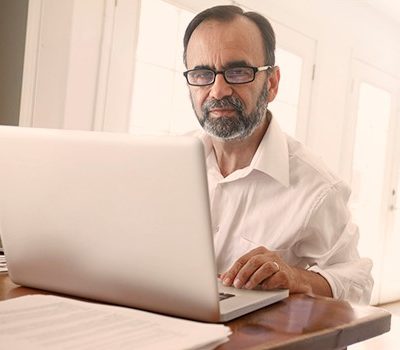 An older man sitting at a table while using a laptop