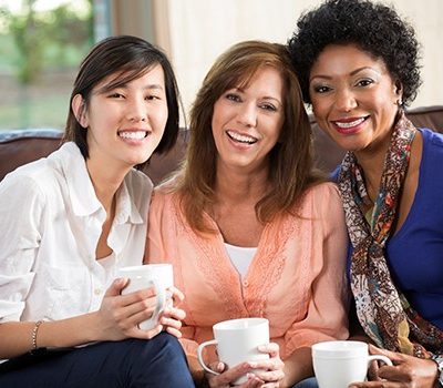 Three women smiling while holding coffee cups