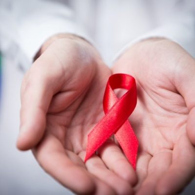 A pair of hands holding a red ribbon commemorating World AIDS Day