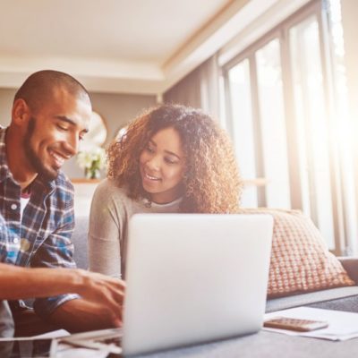 A couple sitting on a couch while using a laptop