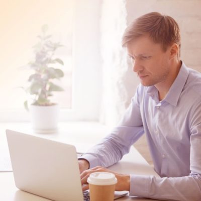 A man sitting at a table drinking coffee while using a laptop