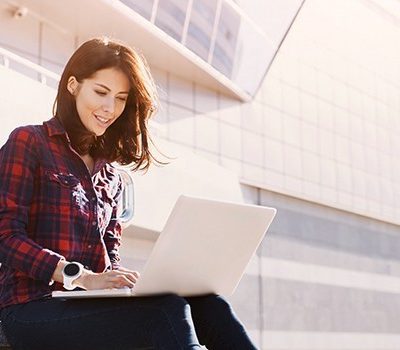 A woman sitting on a bench while using a laptop