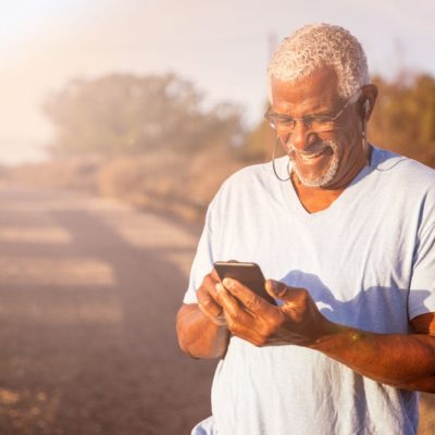 An older man using a cellphone while on a path by a beach