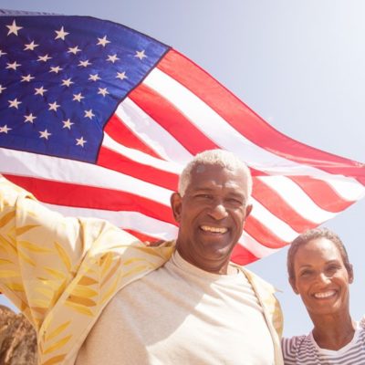 An older couple smiling for the camera while holding an American flag above their heads