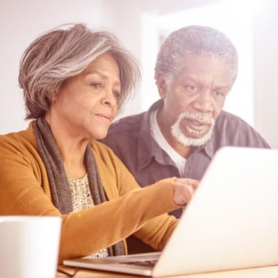 An older couple looking at a laptop while drinking coffee