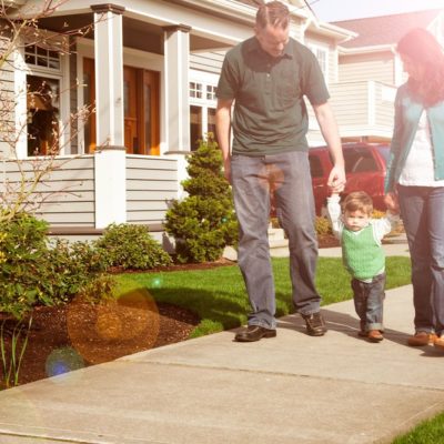 A husband and wife holding their son's hands while they walk down a neighborhood sidewalk