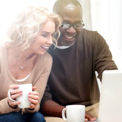 An older couple drinking coffee while looking at a laptop