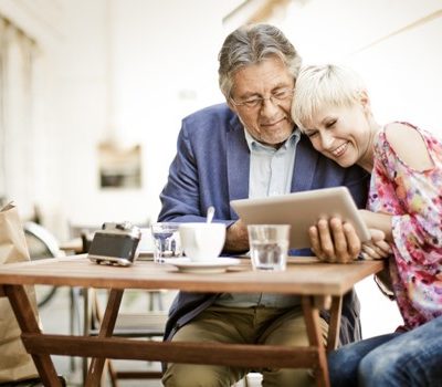 An older couple sitting a table while looking at a tablet device