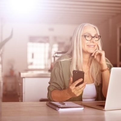 An older woman using a laptop and cell phone