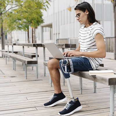 Contemplating man with artificial limb using laptop while sitting on bench in city