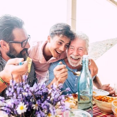 A grandfather, father, and son embracing one another at breakfast.