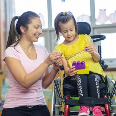 a child playing with her blocks while in a wheelchair with her mother helping.