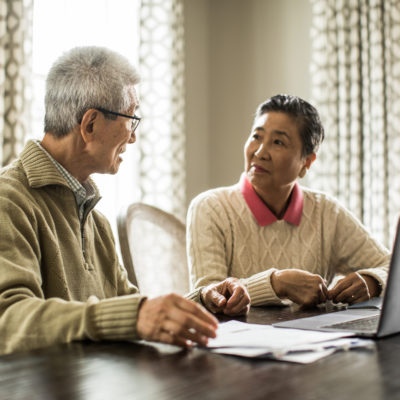 An elderly man and woman looking at each other while sitting at a table.