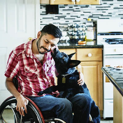 Smiling man in wheelchair having face licked by dog while hanging out in kitchen