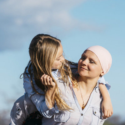 A woman with cancer is next to her daughter. A girl is hugging a woman happy