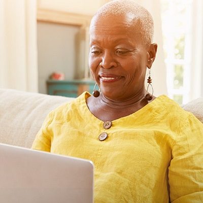 person in yellow shirt reviewing information on a laptop while sitting on a couch