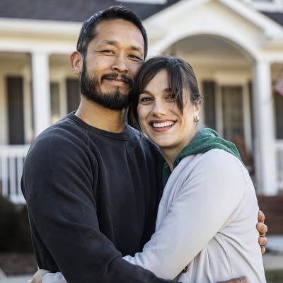 A couple embracing while standing outside their home.