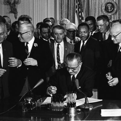 A photo of Lyndon B. Johnson signing the Civil RIghts Act. Martin Luther King Jr. is also pictured behind Johnson.